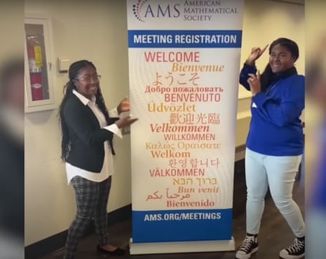 Two teens stand next to a sign for the American Mathematical Society meeting.