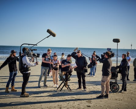 Frith on set on a beach surrounded by camera and microphone operators