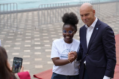 A teenaged African girl poses for a photo clasping hands with a bald European man in a dark suit