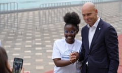 A teenaged African girl poses for a photo clasping hands with a bald European man in a dark suit
