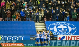 Wigan players mob Will Grigg after his 79th-minute effort put them ahead against high-flying Manchester City.