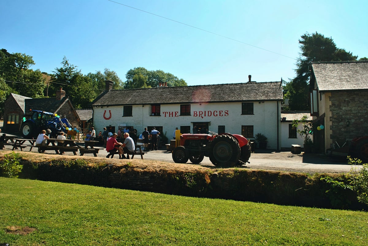 A low whitewashed pub with outdoor seating and a tractor in front of it