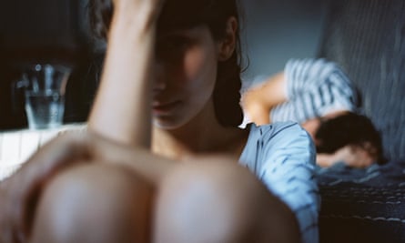 Woman sitting on the floor as a man sleeps in bed behind her