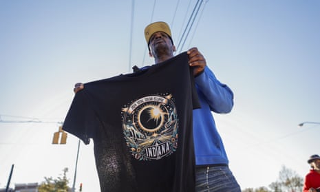 A man holding up a black T-shirt with an eclipse design and the words "2024 total solar eclipse, Indiana" on it