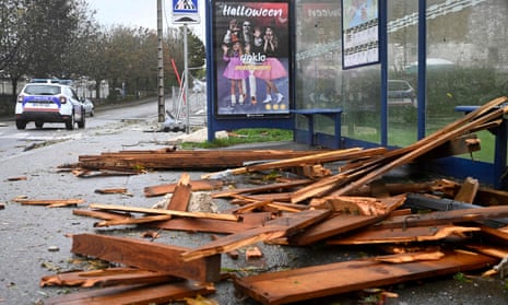 A scattered pile of broken pieces of wood, possibly from a fence, strewn across the pavement by a bus stop