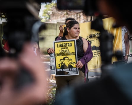 A woman stands in front of yellow banners holding a sign.