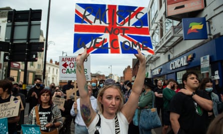 A group of anti-racism protesters walking down a street, with a young woman at the front carrying a union jack with the words ‘Racists not welcome’
