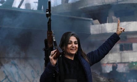 A woman with a rife raises her hand in a victory sign.