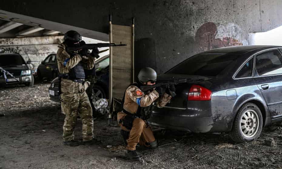 Ukrainian servicemen aim with their weapons at a moving car from a position under a destroyed bridge in the city of Irpin, northwest of Kyiv