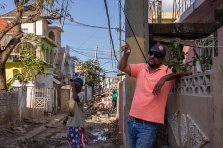 man in coral polo leans against fence, pointing