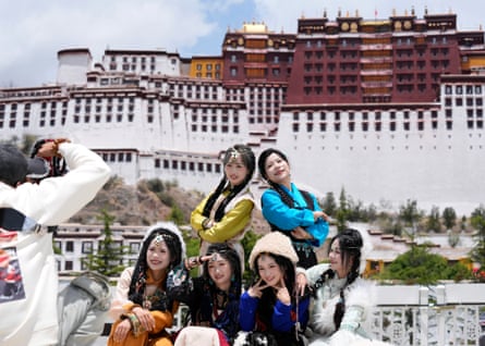Six young Chinese women wearing what appears to be traditional dress adopt exaggerated poses in front of a huge castle-like palace