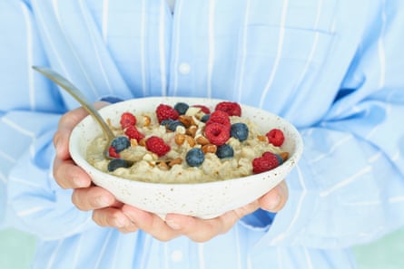 Faceless woman holds in hands breakfast, oatmeal porridge with berries and nuts, healthy food, proper nutrition. Sunshine, early morning, quiet home environment. Side view