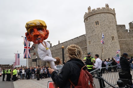 An anti-Trump protester with blond dreadlocks holds up a papier-mache puppet of the president