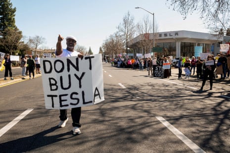 a person holds a sign that reads 'don't buy Tesla'