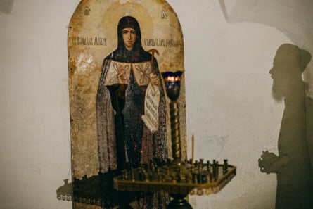 The silhouette of a bearded Orthodox monk praying before an icon with candles in front of it