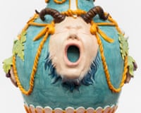 Detail of a ceramic vase shaped like a face with an open mouth, decorated with turquoise glaze and orange rope details