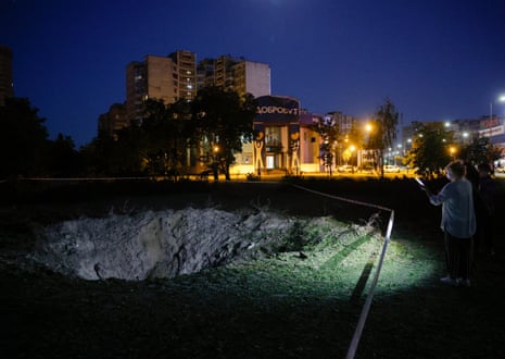 People look at a crater at the site of a Russian missile strike in Kyiv, Ukraine.