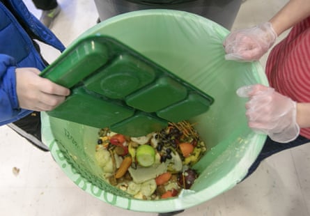 A child dumps food from a green tray into a green food waste can.