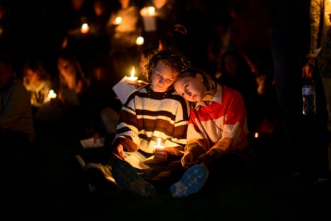 Two people sit close together holding lit candles during a vigil crowd at night