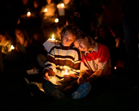 Two people sit close together holding lit candles during a vigil crowd at night