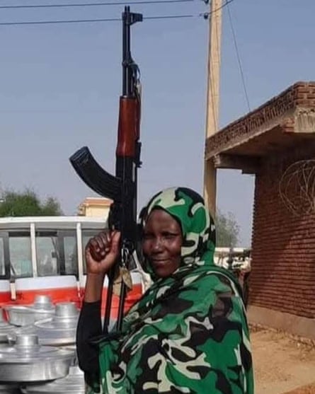 Sāra Bakhit holds a rifle in the air wearing a camouflage headscarf