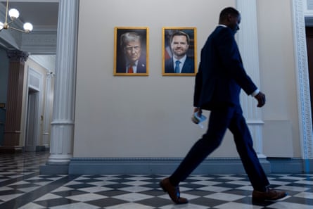 Man in suit walking past portraits of Donald Trump and JD Vance at the White Houseon a black and white chequered corridor floor