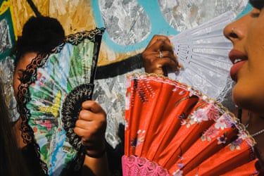At Notting Hill carnival, people hold ornate folding fans against a graffiti backdrop