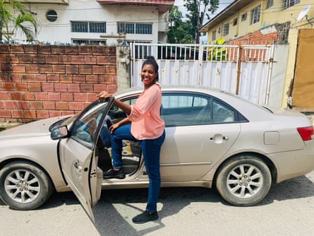 Lilian Ezeugwu gururla arabasının yanında duruyor ve sürücü kapısını açık tutuyor