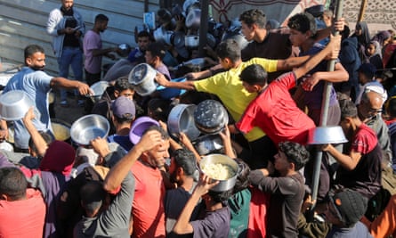 People push forward, holding out empty containers, as they wait to receive food