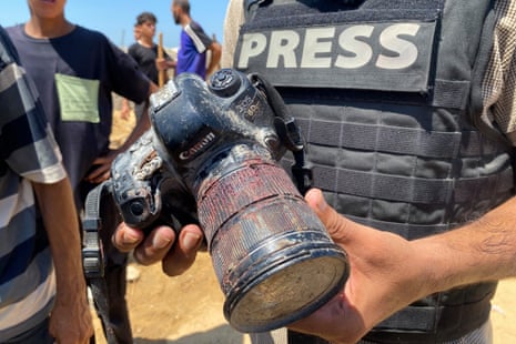 A person in a press vest holds a damaged and blood-stained camera