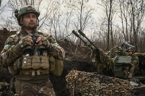 A Ukrainian serviceman (L) looks on and holds binoculars next to another sitting on an anti-air gun near Bakhmut.