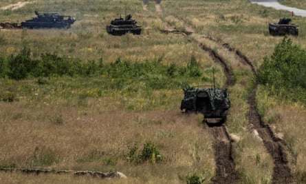 De la fumée monte alors qu'un char, un véhicule blindé de déminage et un véhicule blindé se dirigent vers les positions ennemies lors d'un exercice d'entraînement
