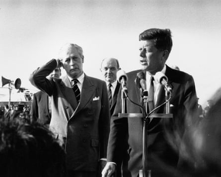 John F Kennedy at an open-air conference microphone, Harold Macmillan beside him with a hand held to his ear
