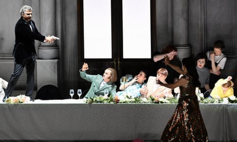 Jonas Kaufmann standing on a table pointing a gun at the diners with Anna Netrebko with her arms raised.
