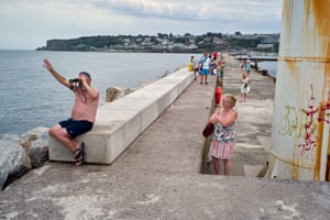 A wife looks at her husband as he waves out to a passing boat through his binoculars at Brixham harbour.