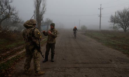 A Ukrainian serviceman speaks with a chaplain while a local person rides a bicycle in a village near Shihurivka