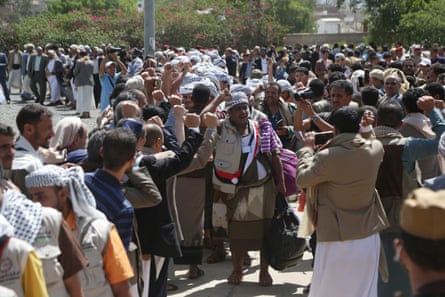 Men raising fists in defiance walk down a road surrounded by people cheering and filming them