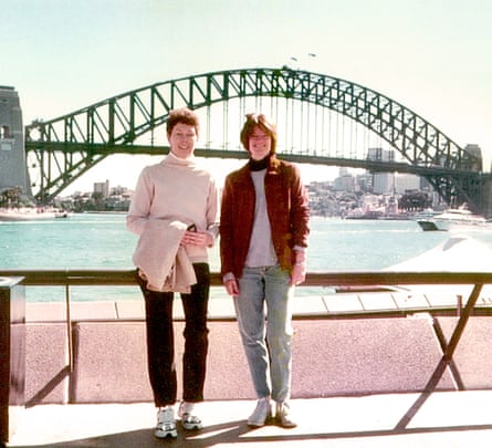 two women smile as they stand next to water in front of bridge