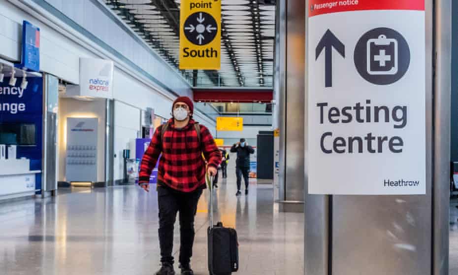 a masked man passes through Heathrow next to Covid testing signs