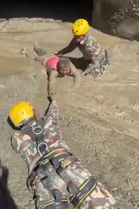 Two rescuers pull a person through the mud.