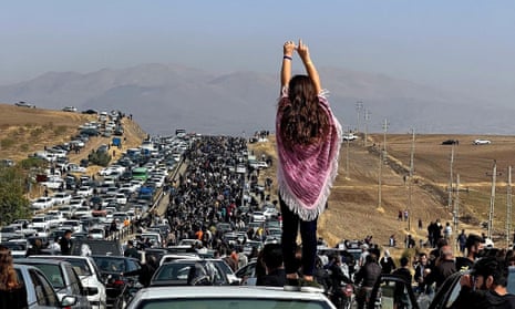 An unveiled woman stands on top of a vehicle as thousands make their way towards Aichi cemetery in Saqez, Mahsa Amini's home town.