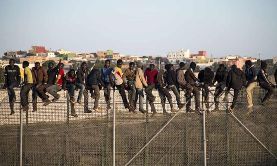 People sit on a border fence separating Melilla from Morocco