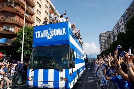 Supporters cheer along a street as Real Sociedad players and staff celebrate atop an open-top bus during a parade in San Sebastián
