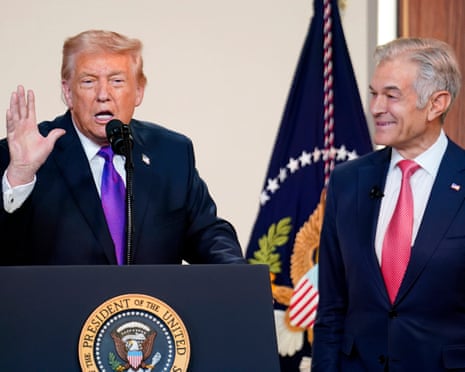 a man speaks into a microphone at a lectern as another man stands nearby smiling in his direction