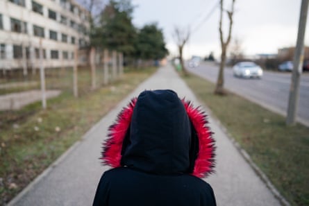 A child wearing a hooded coat walks along a pavement in an urban environment