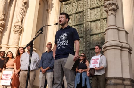 a man wearing a shirt that reads ‘lift the siege on Gaza’ speaks into a microphone
