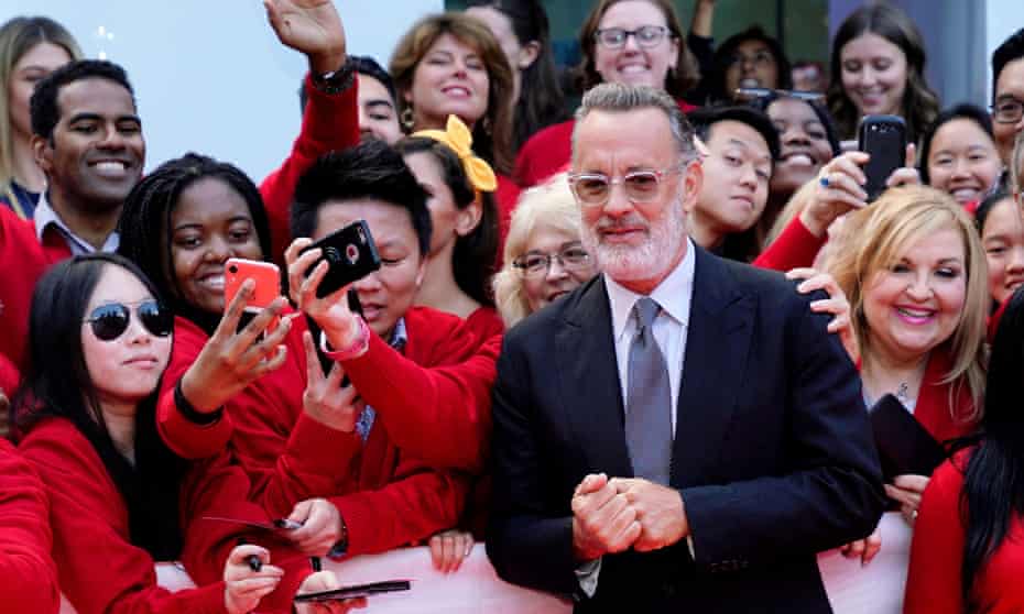 Hanks, bearded, wearing glasses, clutching hands together,  in front of crowd of well-wishers all dressed in red