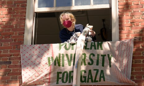 An activist in the US uses keffiyeh scarves tied together to hoist a banner through an upper floor window of a Rhode Island School of Design building they have partially taken over Tuesday, May 7, 2024, at RISD, in Providence, R.I.