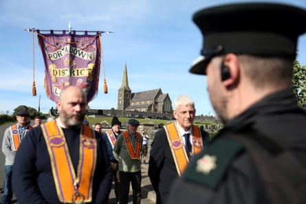 Several members of the Orange Order stand in front of a member of the PSNI, with Drumcree church in the background.