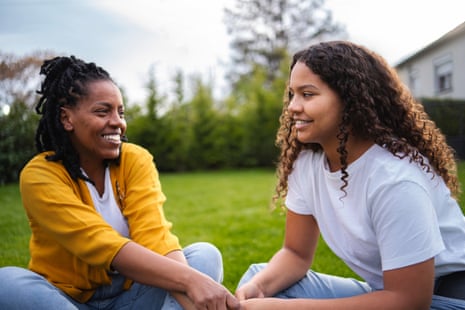 Mother and daughter sitting in grass, holding hands, smiling and talking